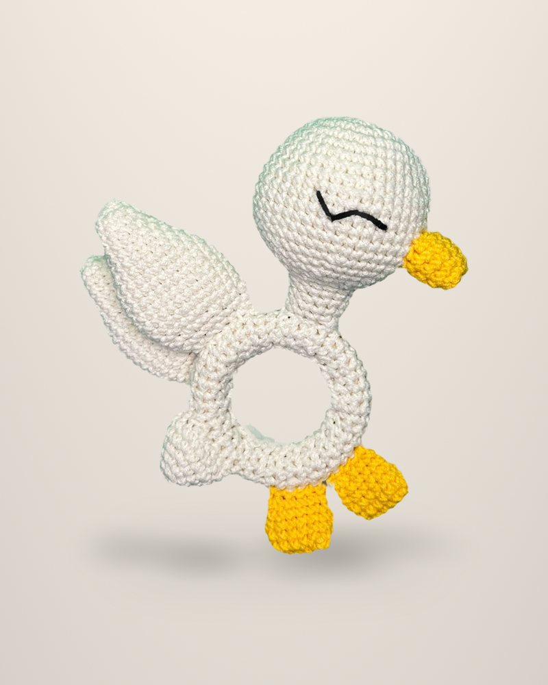 A crocheted ivory duck shaped around a ring, with a yellow beak and feet.
