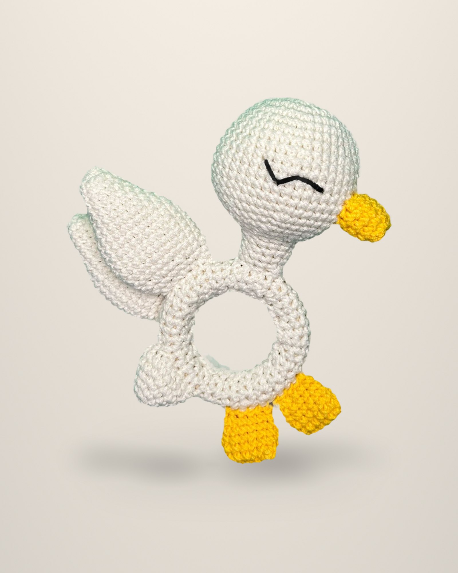 A crocheted ivory duck shaped around a ring, with a yellow beak and feet.