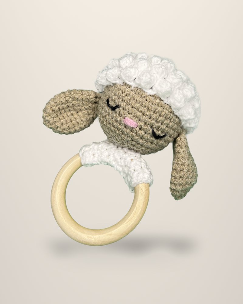 A crocheted sleeping lamb's head with white curls, attached to a pale ring.