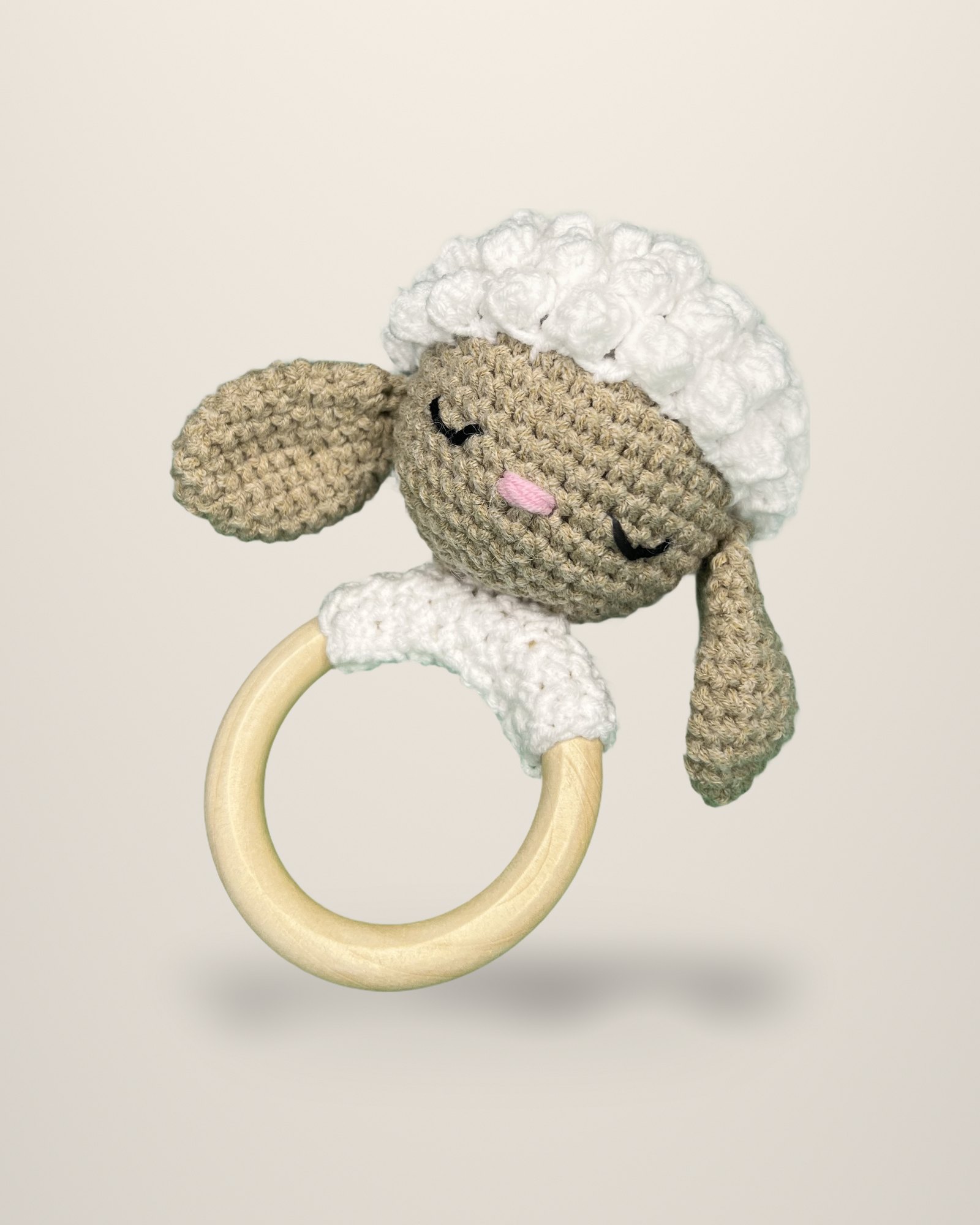 A crocheted sleeping lamb's head with white curls, attached to a pale ring.