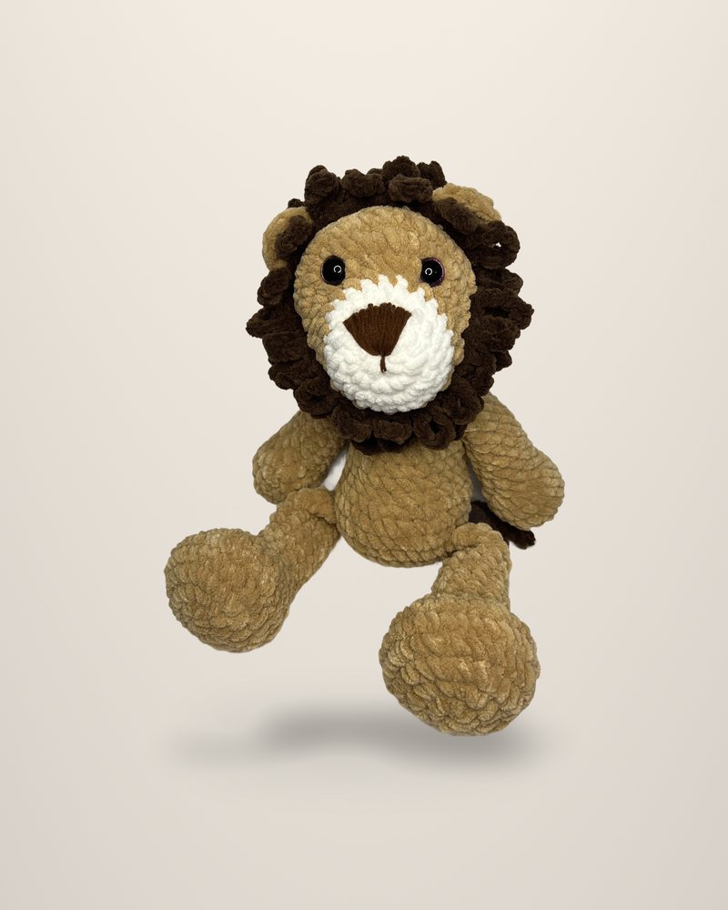 A crocheted lion in honey tones with a dark brown curled mane, seated.