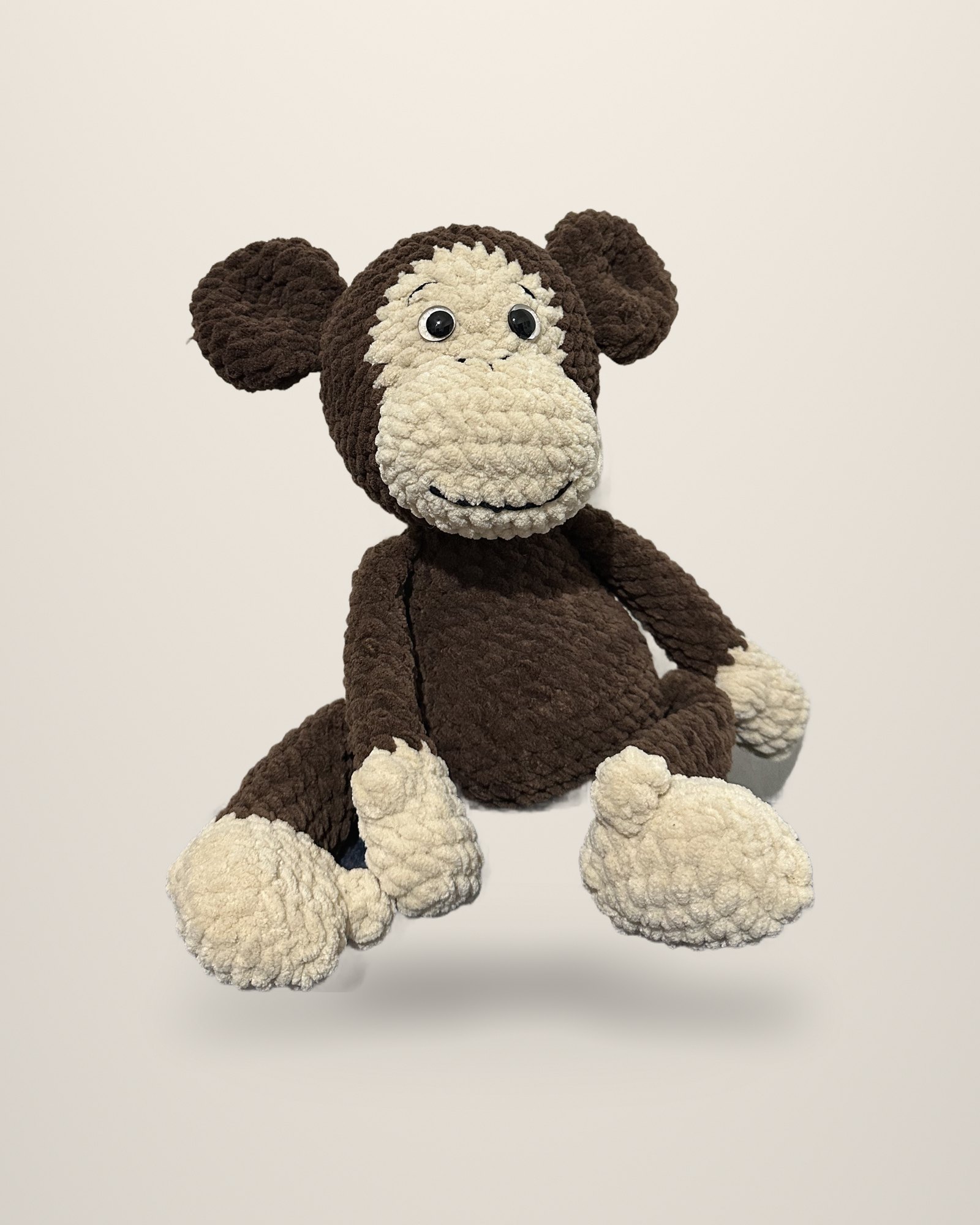 A crocheted monkey in chocolate brown with a cream face, hands and feet, seated.